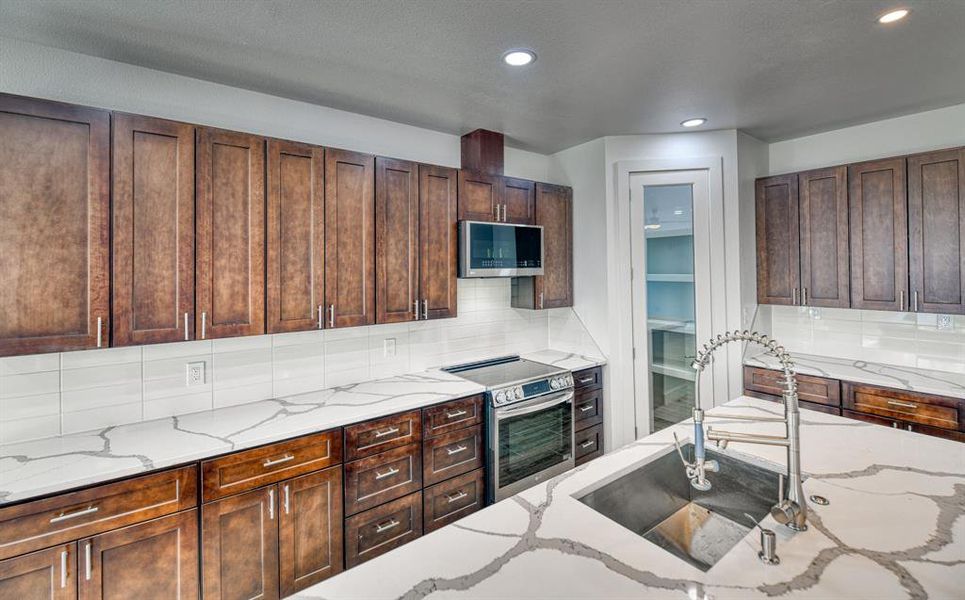 Kitchen with appliances with stainless steel finishes, light stone counters, sink, and backsplash