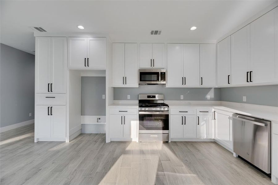 Kitchen with appliances with stainless steel finishes, light wood-type flooring, and white cabinets