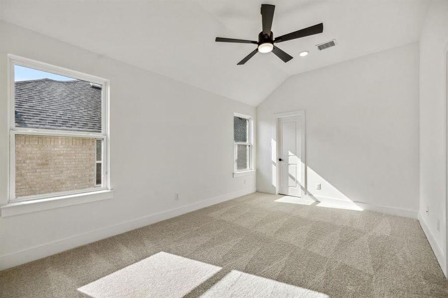 Empty room featuring plenty of natural light, ceiling fan, vaulted ceiling, and light colored carpet