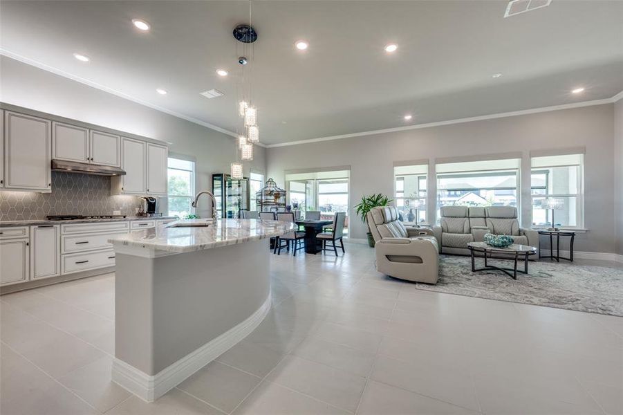 Kitchen with pendant lighting, Dolomite countertops, and a kitchen island with sink, overlooking living room and dining area