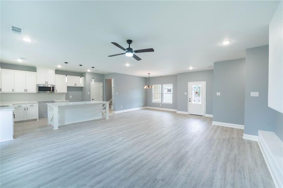 Kitchen with ceiling fan with notable chandelier, a center island, white cabinetry, light hardwood / wood-style floors, and decorative light fixtures