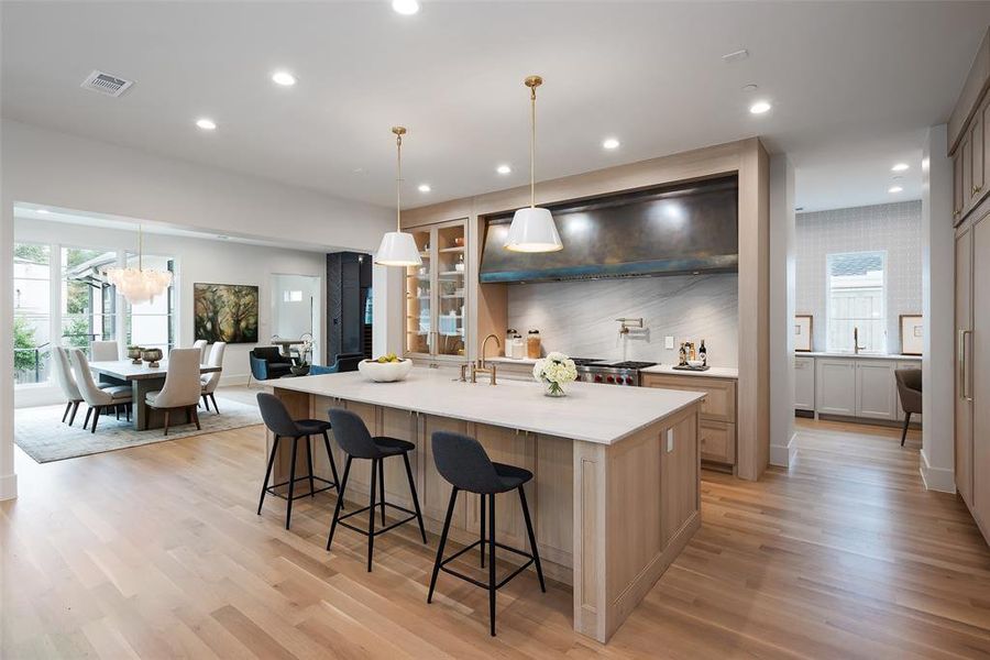Kitchen with decorative light fixtures, light hardwood / wood-style floors, a large island with sink, extractor fan, and a breakfast bar