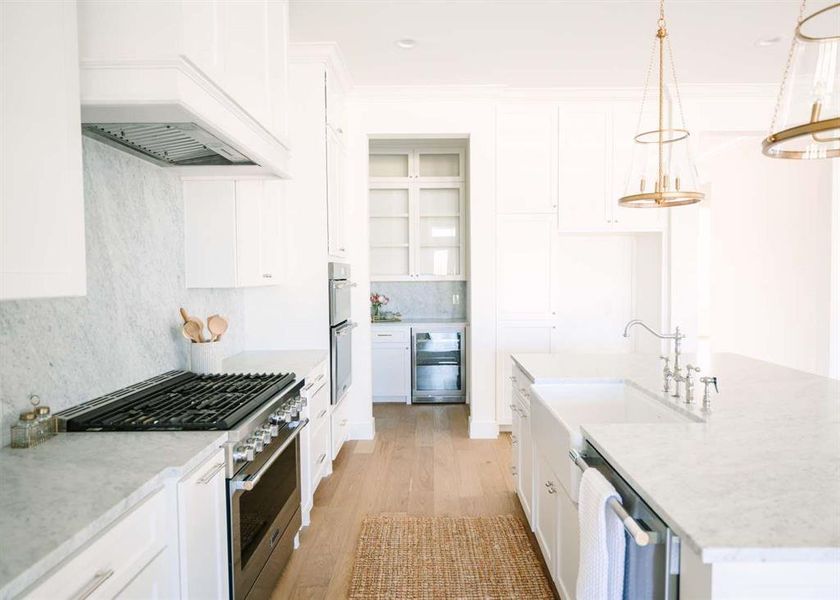 Kitchen with appliances with stainless steel finishes, white cabinetry, an island with sink, pendant lighting, and light hardwood / wood-style flooring