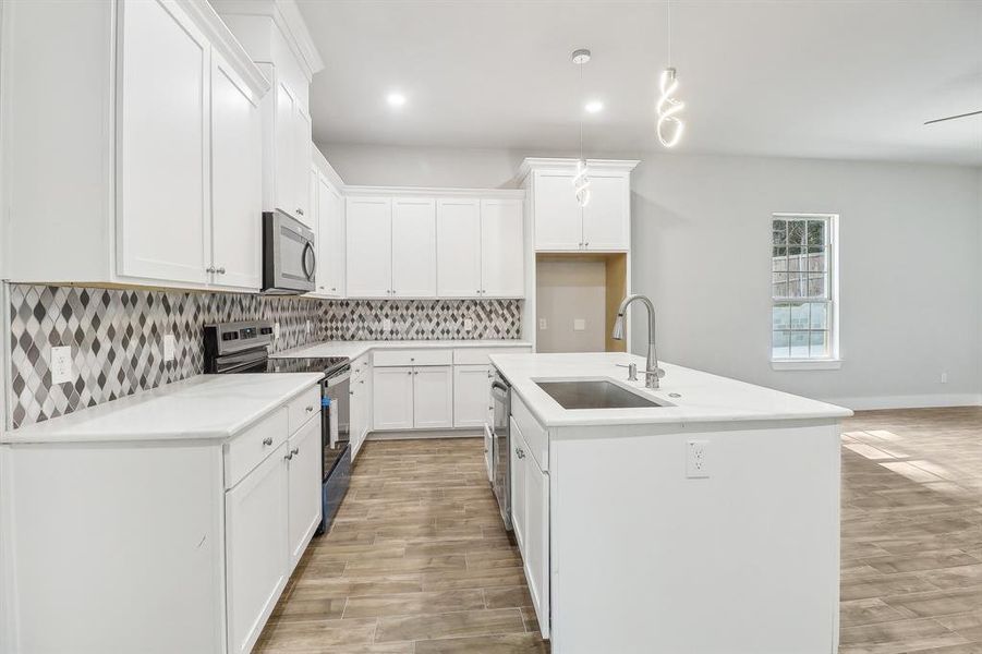 Kitchen featuring appliances with stainless steel finishes, white cabinetry, light hardwood / wood-style flooring, a kitchen island with sink, and sink