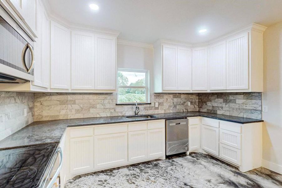 Kitchen featuring backsplash, ornamental molding, stainless steel appliances, sink, and white cabinets