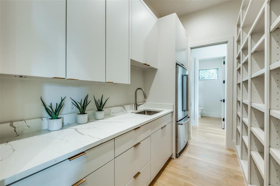 Kitchen with white cabinetry, sink, light stone countertops, high quality fridge, and light hardwood / wood-style floors