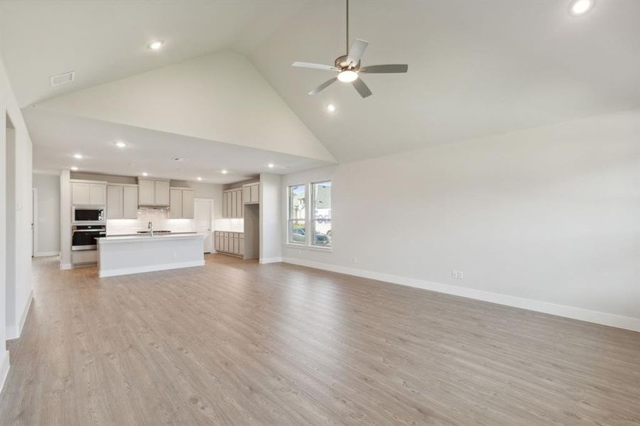 Unfurnished living room featuring light wood-type flooring, high vaulted ceiling, sink, and ceiling fan