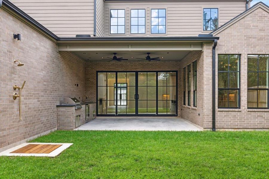 The covered outdoor living area is perfect for entertaining, featuring a built-in grill, sink, and outdoor shower/dog wash. The large sliding glass doors seamlessly blend indoor and outdoor living, opening up to the lush backyard.