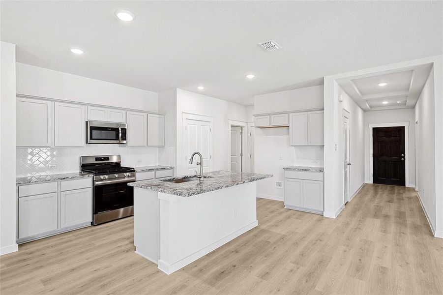 Kitchen featuring appliances with stainless steel finishes, light hardwood / wood-style floors, a center island with sink, and light stone countertops