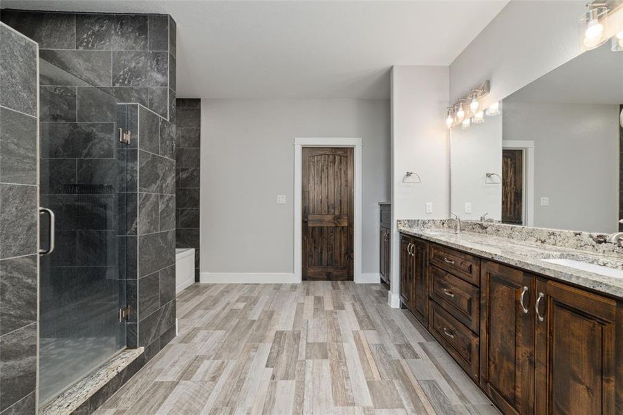 Enter into the spacious primary bathroom, where a grand walk-in shower awaits behind a sleek glass door, surrounded by elegant dark grey tiles that exude modern sophistication. Expansive granite counters provide ample space, perfect for your morning routine in this luxurious retreat.