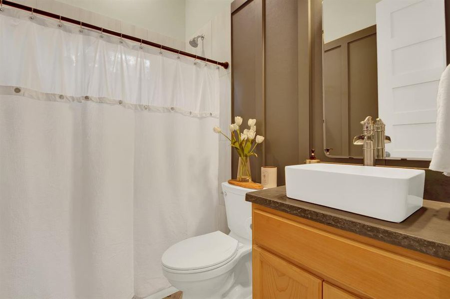 This bathroom features a modern rectangular vessel sink atop a wooden vanity, a toilet, and a shower. The space is accented by neutral tones and clean lines, creating a sleek and inviting atmosphere.