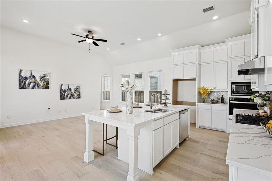 Kitchen featuring light wood-type flooring, a center island with sink, stainless steel appliances, sink, and ceiling fan