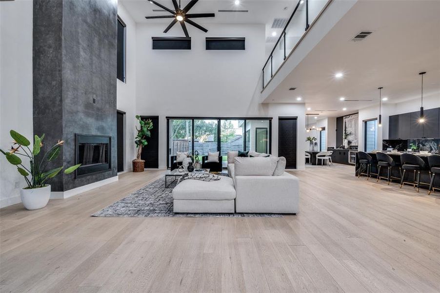 Living room with a large fireplace, a towering ceiling, light hardwood / wood-style flooring, and ceiling fan with notable chandelier