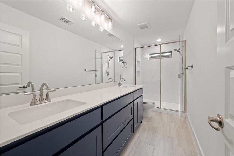 Bathroom with dual vanity, toilet, tile patterned floors, and walk in shower