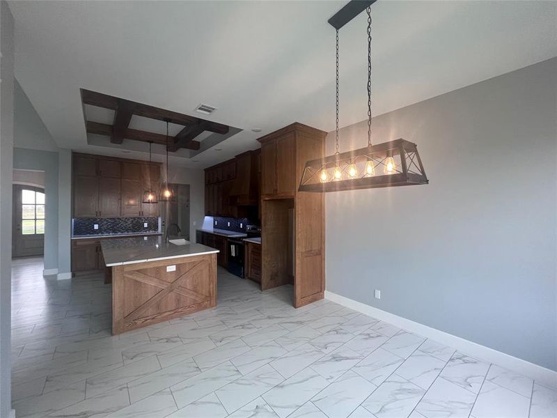 Kitchen with backsplash, a notable chandelier, an island with sink, and hanging light fixtures