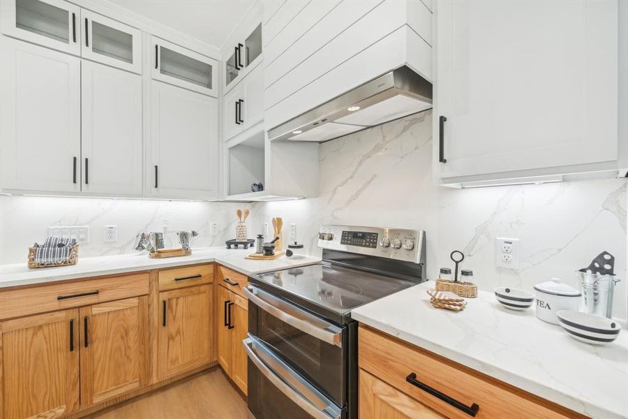 Kitchen with backsplash, light hardwood / wood-style flooring, white cabinetry, premium range hood, and electric stove