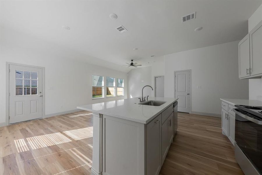 Kitchen with stainless steel range with electric cooktop, a kitchen island with sink, light wood-type flooring, and sink