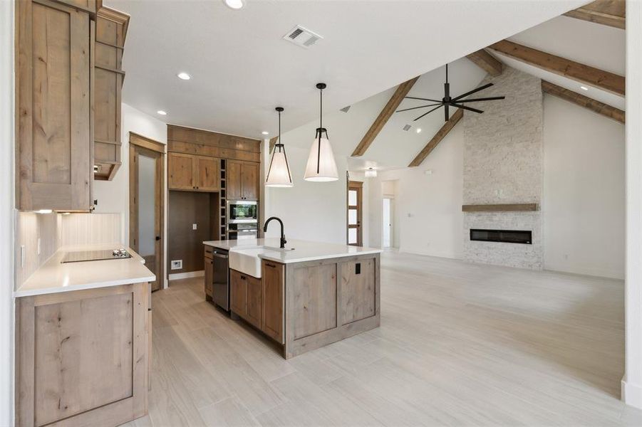 Kitchen featuring decorative light fixtures, ceiling fan, vaulted ceiling with beams, a center island with sink, and a stone fireplace