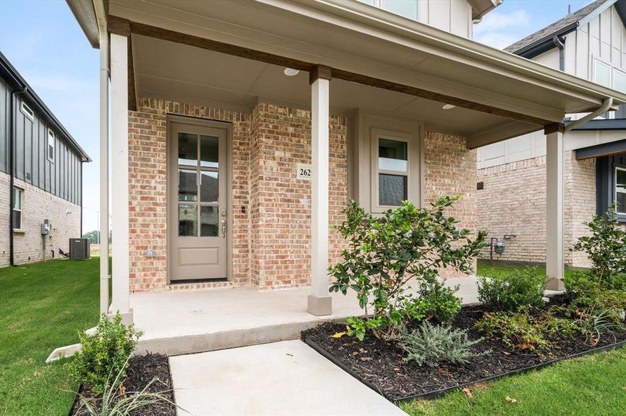 Entrance to property featuring covered porch, central AC, and a yard