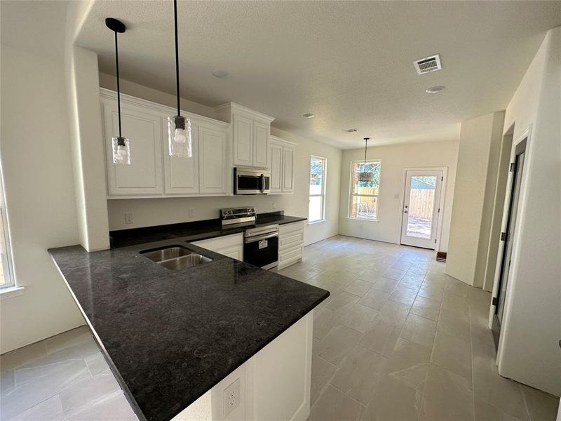 Kitchen with hanging light fixtures, stainless steel appliances, kitchen peninsula, sink, and white cabinets