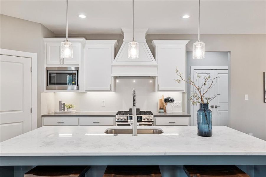 Kitchen with premium range hood, a center island with sink, a breakfast bar, and stainless steel microwave