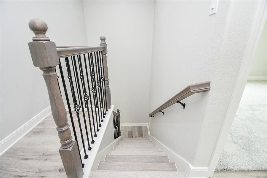 This photo showcases a modern staircase with elegant wood finishes and decorative metal balusters, leading down to a carpeted area. The light color palette creates a fresh and airy feel.