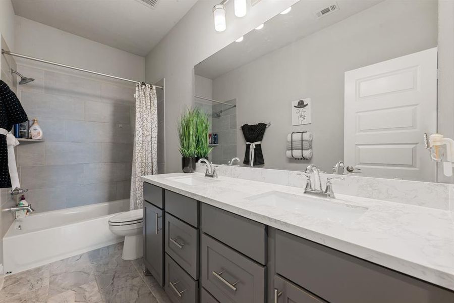 Secondary bath features tile flooring, bath/shower combo with tile surround, dark cabinets, beautiful light countertops, mirror, dark, sleek fixtures and modern finishes.