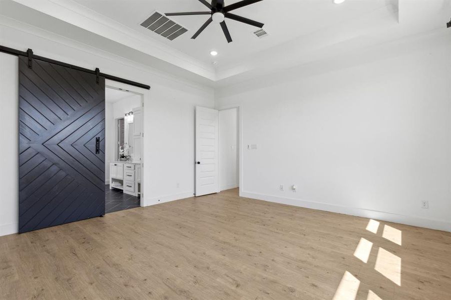 Unfurnished room featuring a barn door, a tray ceiling, ceiling fan, and light hardwood / wood-style flooring