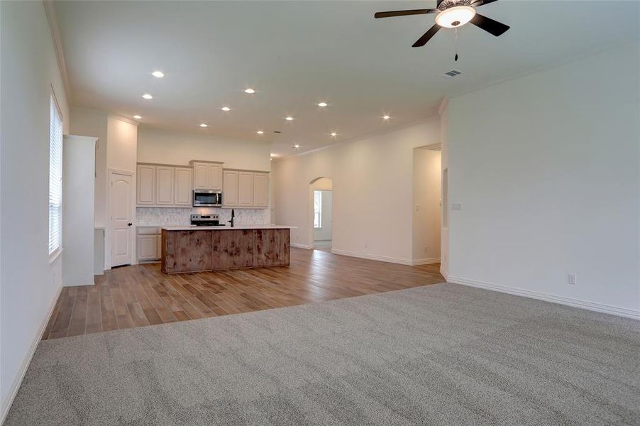 Kitchen featuring light colored carpet, ornamental molding, an island with sink, and stainless steel appliances