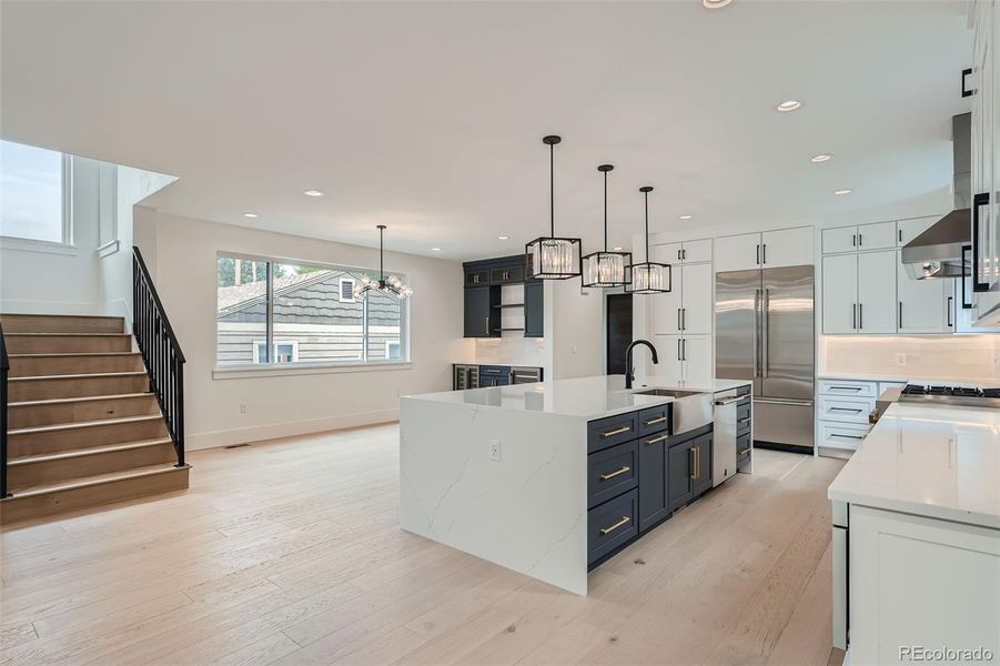 Chef's kitchen showcasing a massive quartz waterfall island, complemented by sleek quartz countertops, undercabinet lighting, stainless steel refrigerator/freezer, six-burner gas range, built-in hood vent, dishwasher, and microwave.