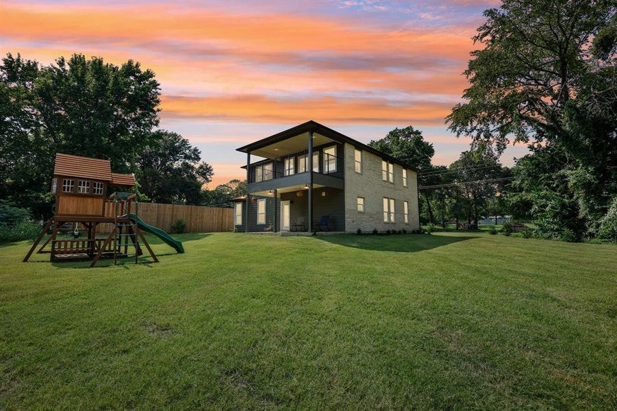 Back house at dusk featuring a balcony, a yard, and a playground