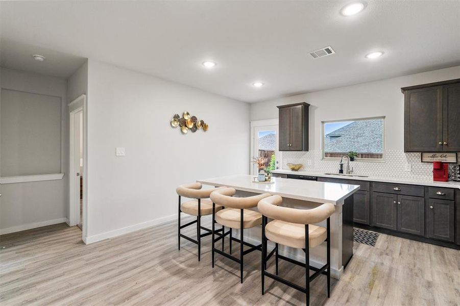 Kitchen featuring decorative backsplash, sink, a breakfast bar, dark brown cabinetry, and light wood-type flooring