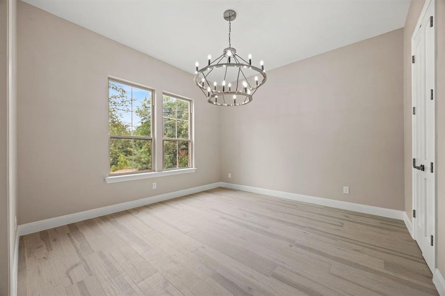 Empty room with light hardwood / wood-style floors and an inviting chandelier