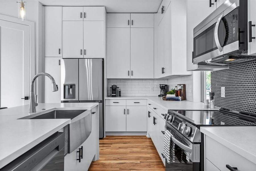 Kitchen with stainless steel appliances, light hardwood floors, backsplash, and white cabinetry