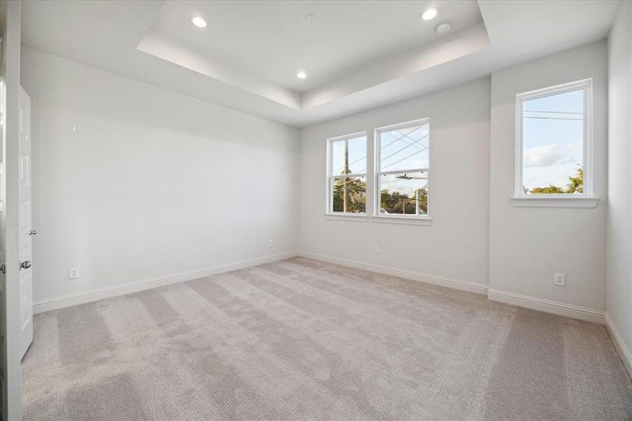 Located on the third floor, this serene primary bedroom offers a peaceful retreat with its soft neutral palette, plush carpeting, and tray ceiling detail. Large windows flood the space with natural light, creating a bright and airy ambiance. With plenty of space for furniture and design personalization, this room provides a perfect sanctuary at the end of the day.