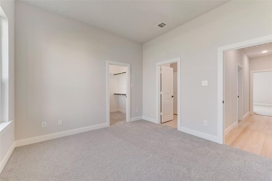 Unfurnished bedroom with light colored carpet, a closet, ensuite bathroom, and a walk in closet