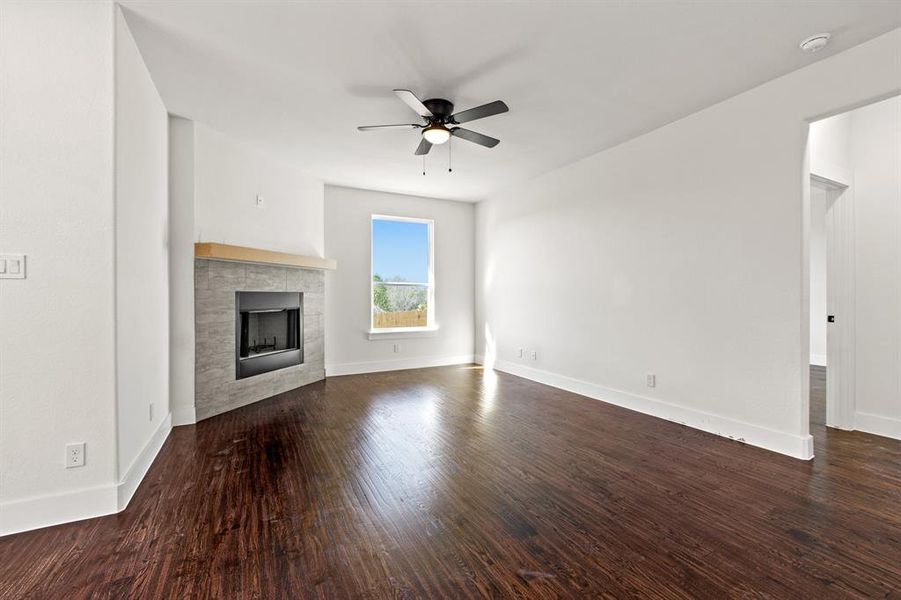 Unfurnished living room with hardwood / wood-style floors, ceiling fan, and a tiled fireplace