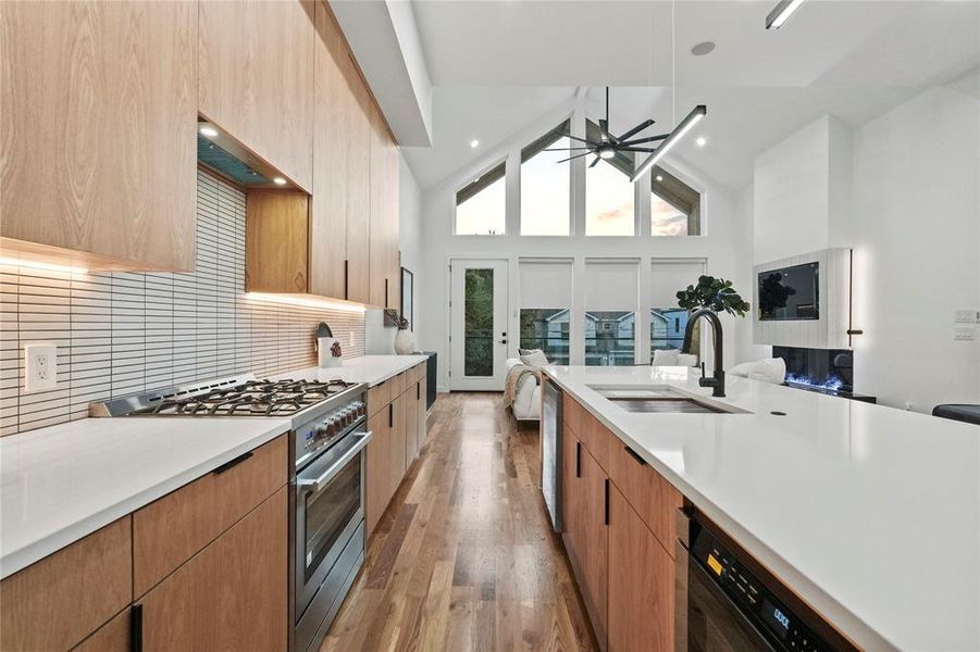 Kitchen with light hardwood / wood-style floors, stainless steel appliances, sink, high vaulted ceiling, and decorative backsplash