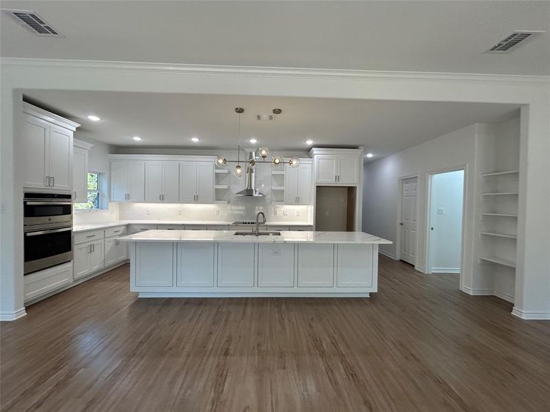 Kitchen with wood-type flooring, a center island, wall chimney exhaust hood, pendant lighting, and white cabinets