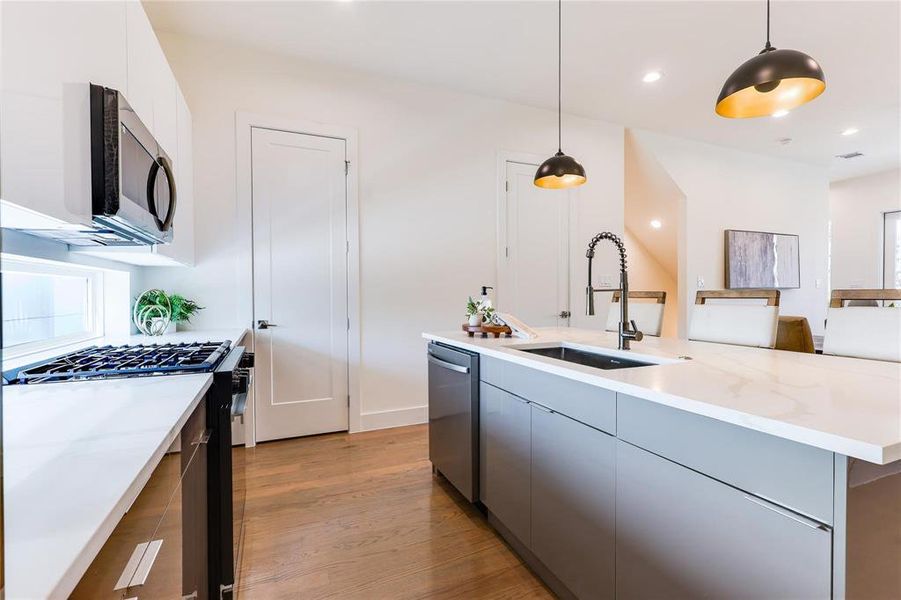 Kitchen with appliances with stainless steel finishes, hanging light fixtures, white cabinets, light wood-type flooring, and sink