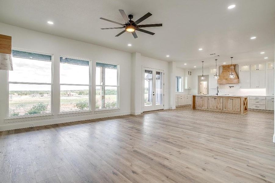 Unfurnished living room with ceiling fan, light wood-type flooring, and french doors