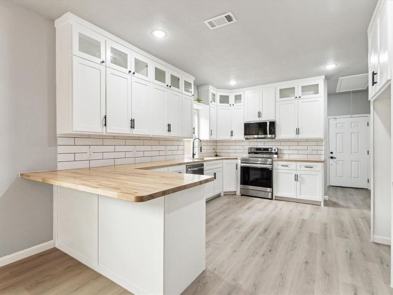 Kitchen featuring light hardwood / wood-style flooring, tasteful backsplash, stainless steel appliances, kitchen peninsula, and white cabinetry