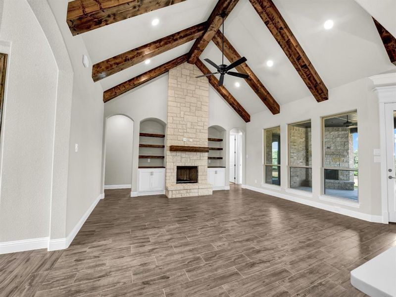 Unfurnished living room featuring a fireplace, beamed ceiling, ceiling fan, dark hardwood / wood-style floors, and high vaulted ceiling