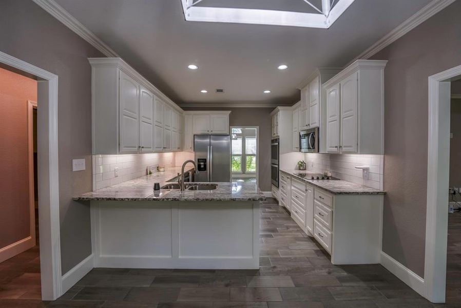 Kitchen featuring appliances with stainless steel finishes, light stone countertops, white cabinetry, double sink, and kitchen peninsula