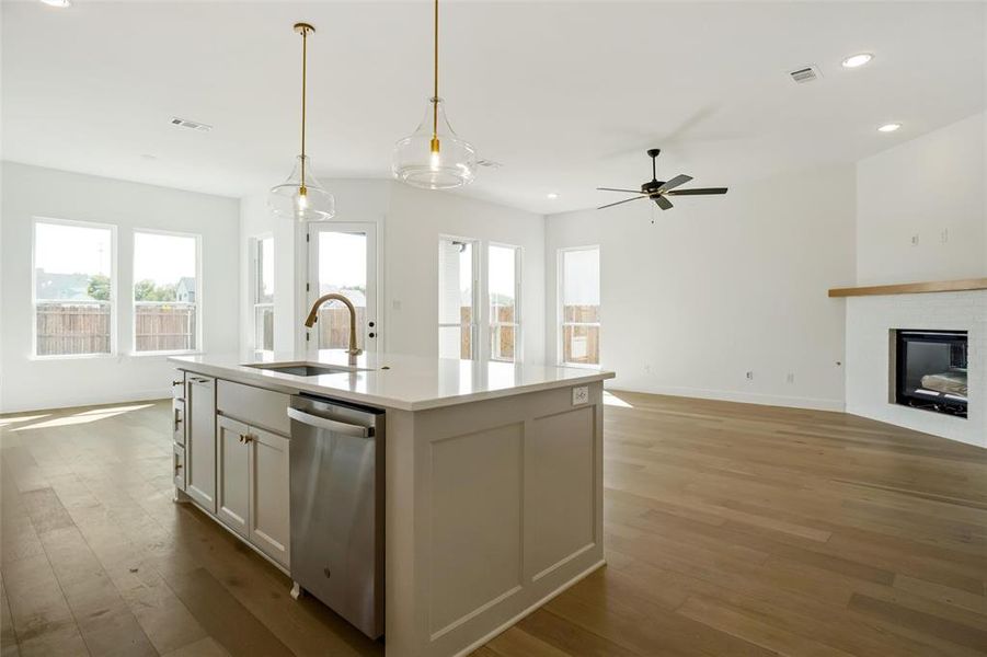 Kitchen featuring sink, hanging light fixtures, stainless steel dishwasher, light hardwood / wood-style flooring, and a kitchen island with sink