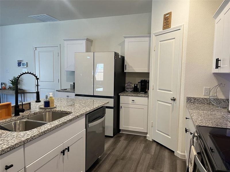 Kitchen featuring light stone countertops, appliances with stainless steel finishes, sink, white cabinets, and dark wood-type flooring