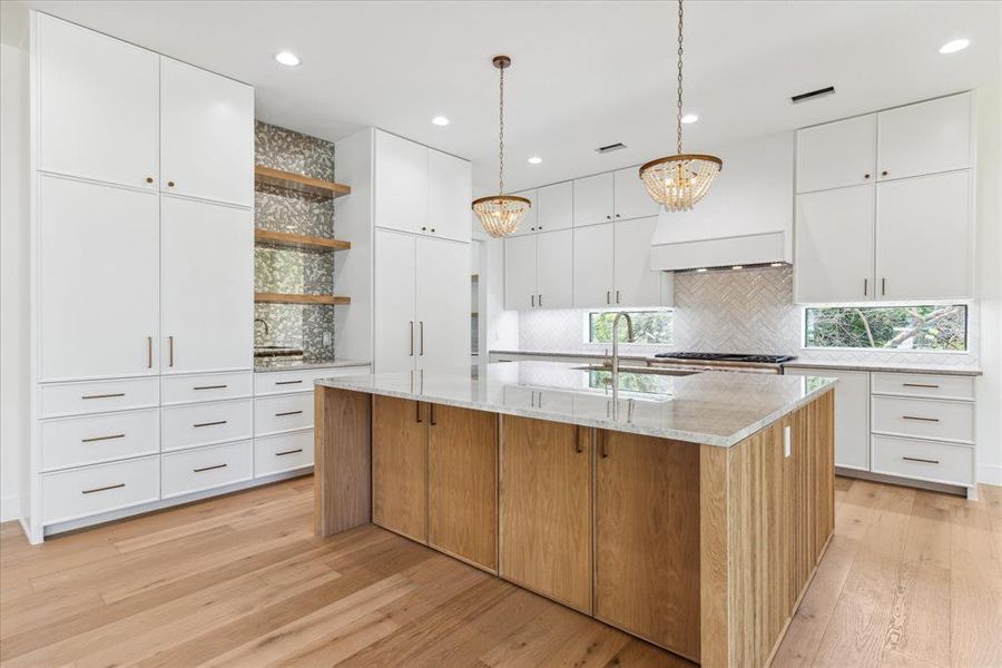 The kitchen boasts floating white oak open shelving with an antique mirror backsplash, enhancing its elegant design. A polished nickel faucet with a pull-down feature complements the stainless steel single basin sink. Open to the breakfast room and living room, the space is further accented by dual designer pendants and a Thermador appliance package.