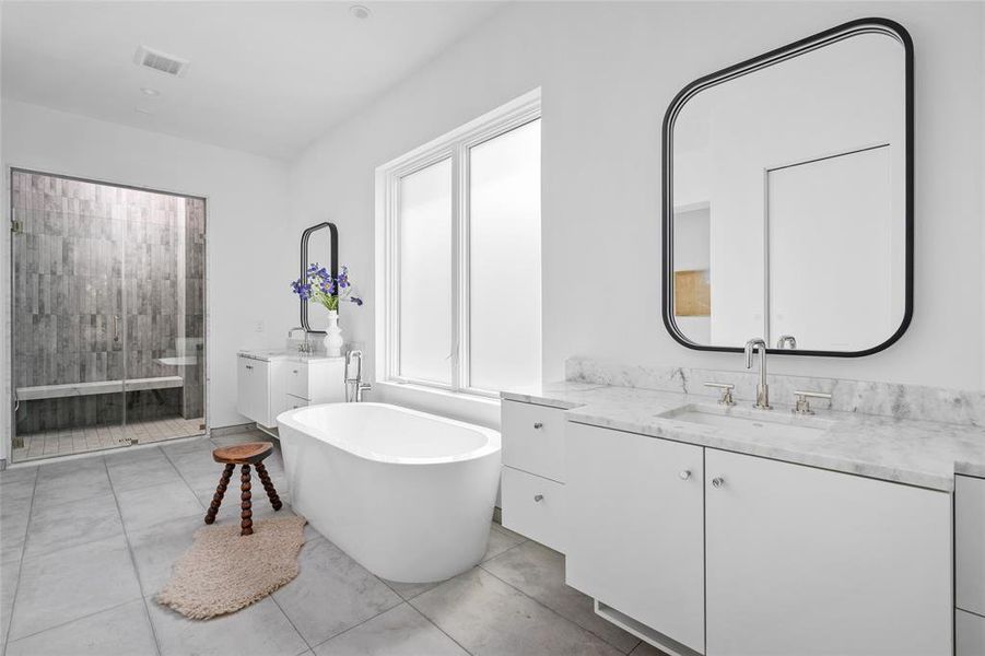 This elegant primary ensuite bath features luxurious limestone floors and baseboards while dual floating vanities are topped with Shadow Storm honed marble counters, offering a refined touch of sophistication.