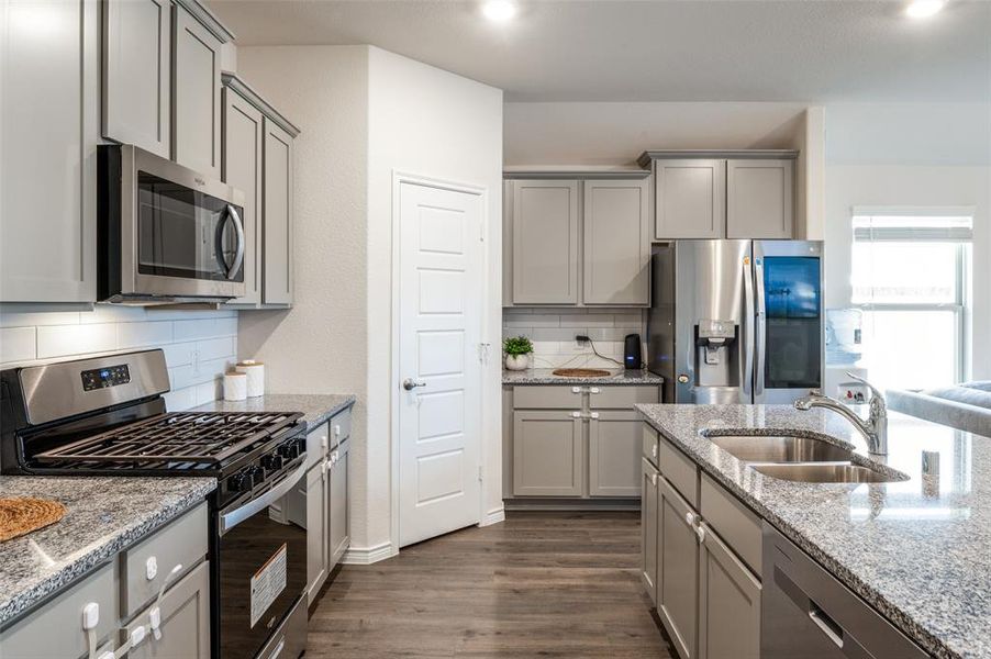 Kitchen with tasteful backsplash, light stone counters, dark hardwood / wood-style floors, sink, and stainless steel appliances