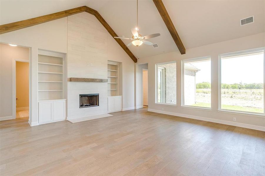 Unfurnished living room with high vaulted ceiling, beamed ceiling, built in features, light hardwood / wood-style flooring, and a tile fireplace